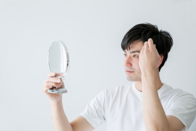鏡を持ってこめかみを気にする男性